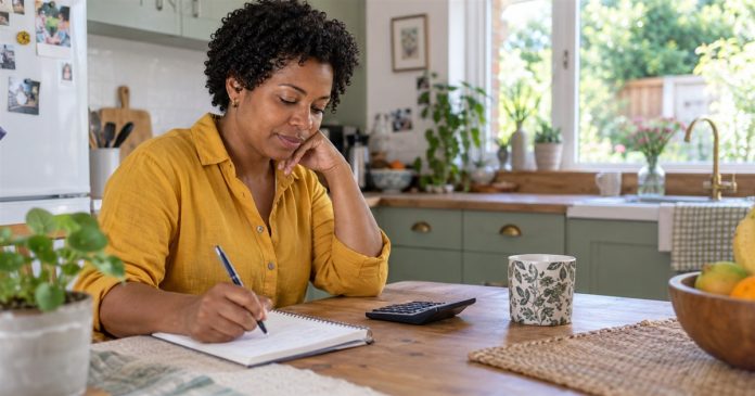 Woman writing in a notebook beside a calculator at her home kitchen table