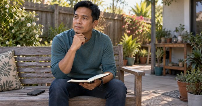 Man reflecting with an open notebook and a face-down phone on a home backyard bench