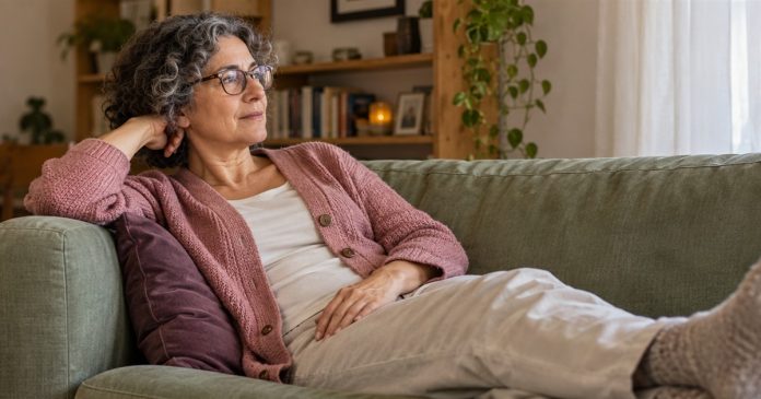 Chronic fatigue and spiritual meaning — everyday rest Woman in a dusty rose cardigan resting on a sage sofa in a home living room