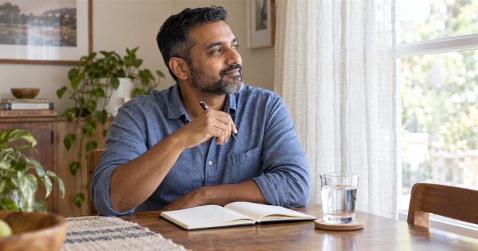 Man pausing with a notebook and glass of water beside a home window