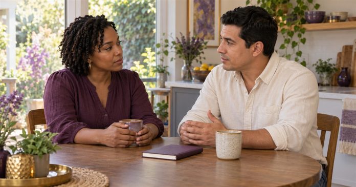 Two adult partners talking calmly at a kitchen table with a notebook and mugs.